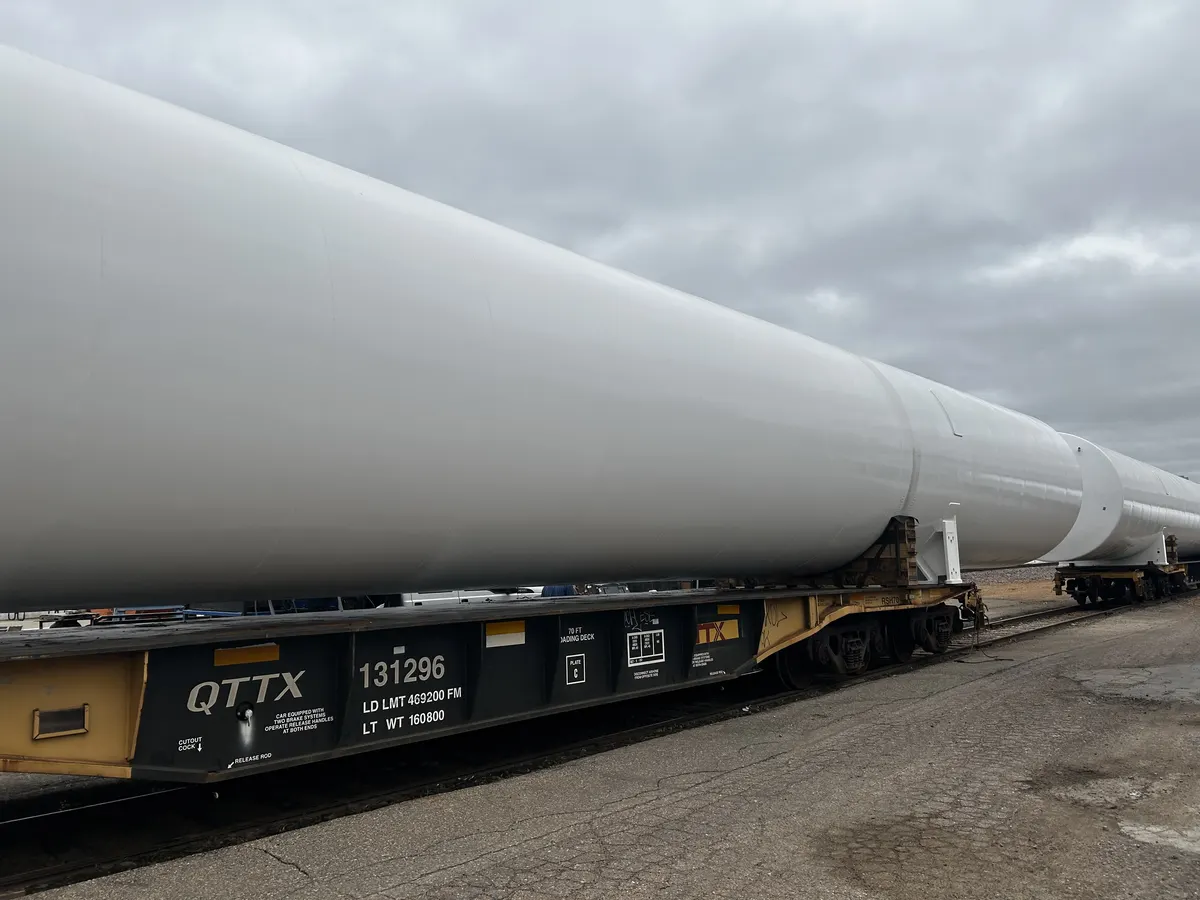 Close-up of a finished GreenER LNG tank loaded on a QTTX heavy-haul rail flatcar — tank diameter visibly wider than the railcar deck