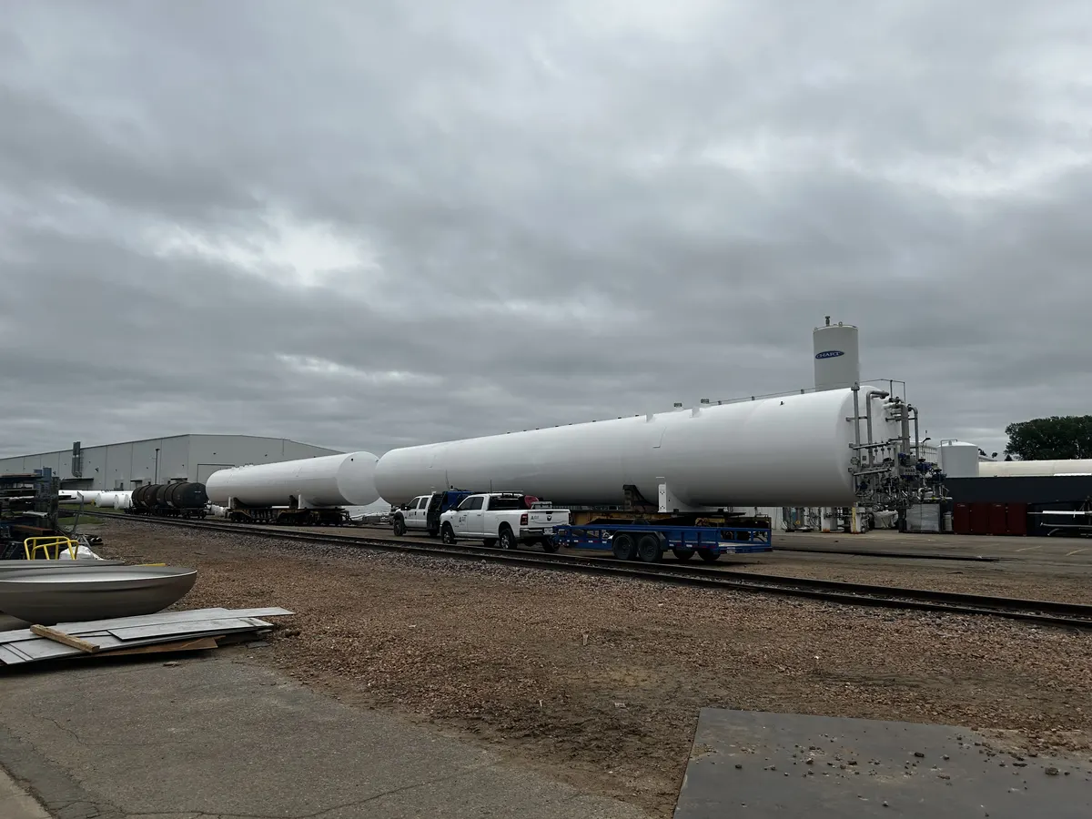 Two finished GreenER LNG tanks staged on rail flatcars at Chart Industries' fabrication yard — pickup truck visible for scale