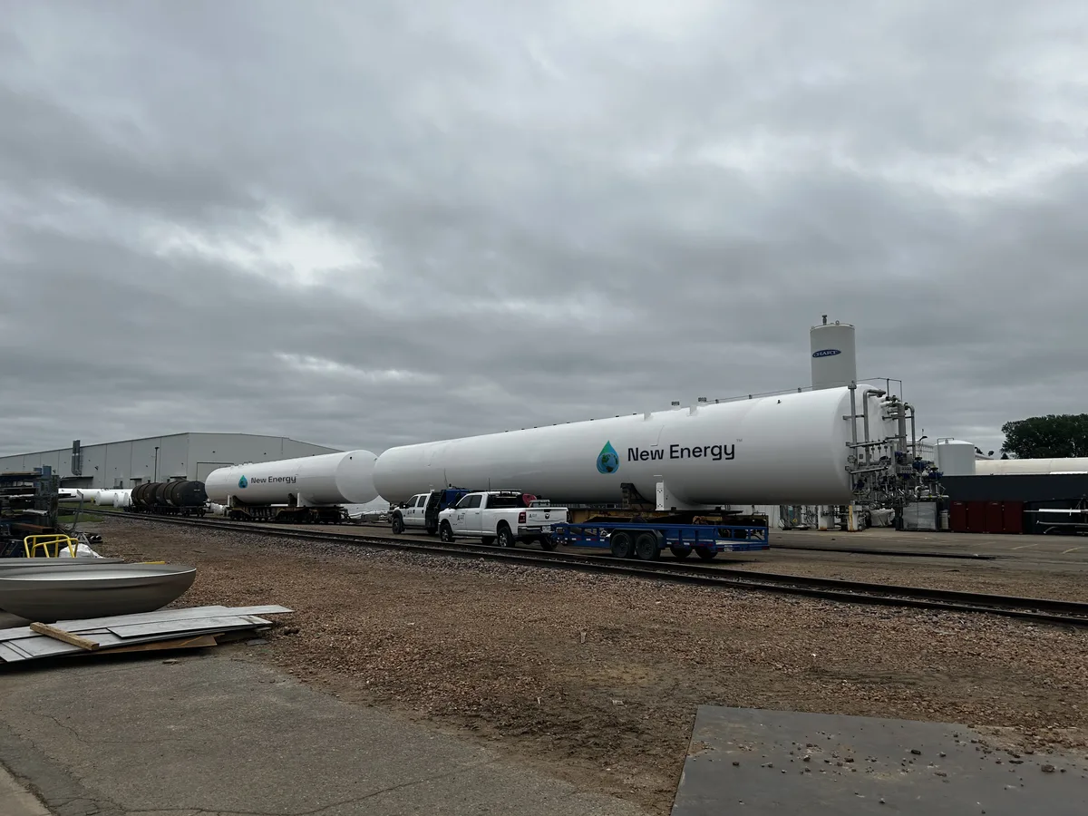 Two finished GreenER tanks carrying the New Energy logo, staged on rail flatcars at the fabrication yard — pickup truck visible for scale